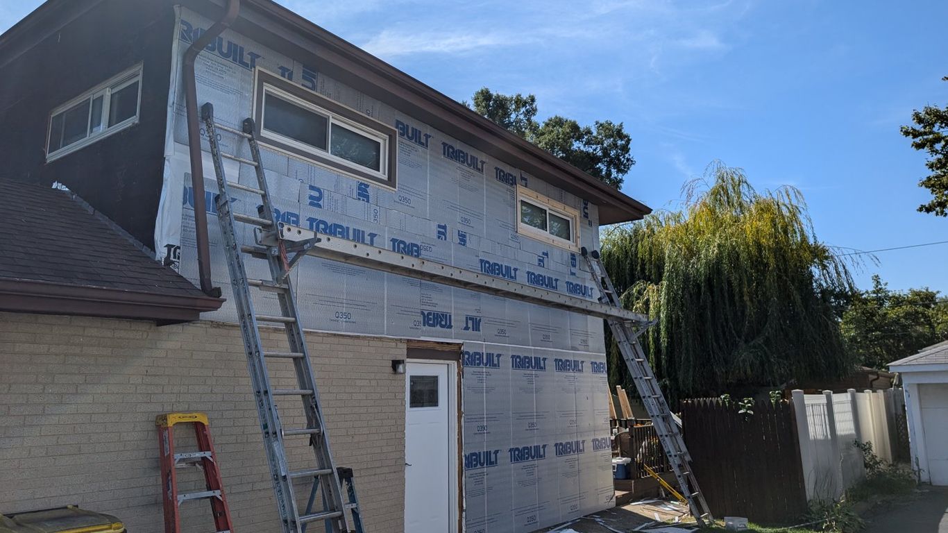 House exterior under construction with new siding and ladders.