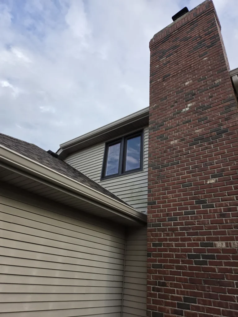 Dark-framed upper window beside a brick chimney on Main Street in Homer Glen